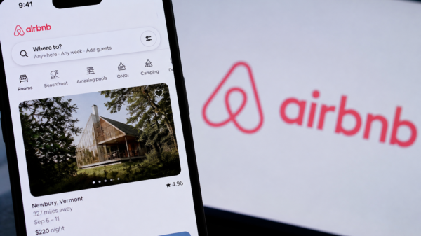 Airbnb app displayed on a smartphone with the company logo visible on a screen behind it.
