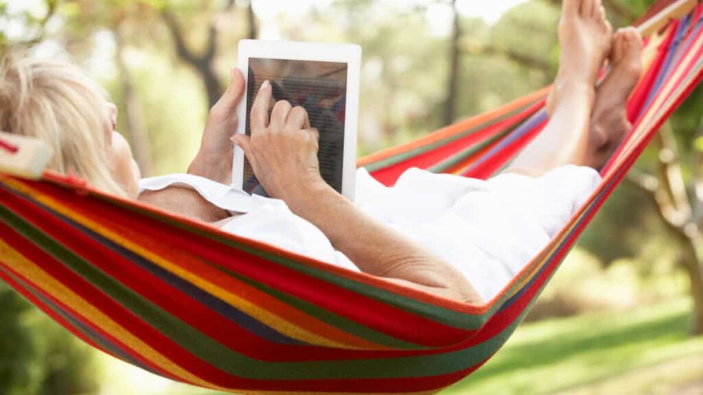 senior relaxes in hammock with e-book