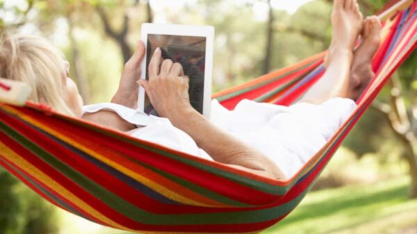 senior relaxes in hammock with e-book