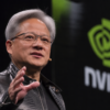 Jensen Huang speaks on stage beside a large Nvidia logo during a technology event.